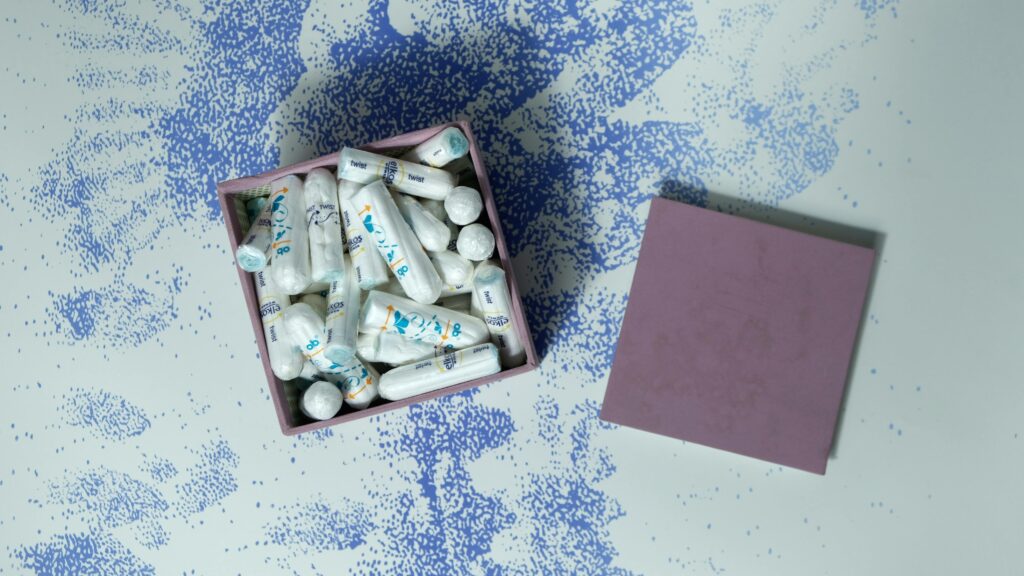 A pink box filled with tampons on a creative speckled blue and white surface.